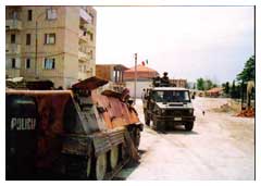 Un veicolo dell'Arma mentre esegue uno dei suoi pattugliamenti. In primo piano, semidistrutto, un blindato della Polizia albanese.